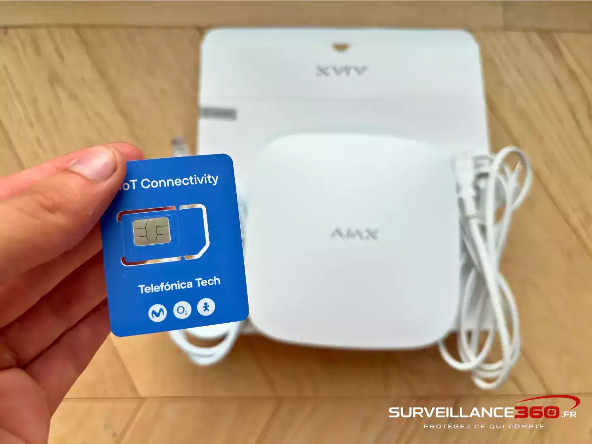 Carte SIM multi-opérateur en main devant une centrale d'alarme Ajax