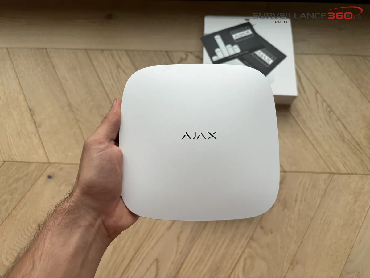 Hub Ajax blanc en main au-dessus de sa boite avant installation